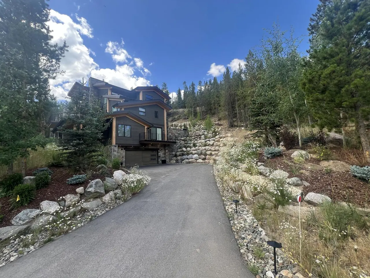 A modern mountain home with boulder retaining walls stepping up the hill beside its driveway